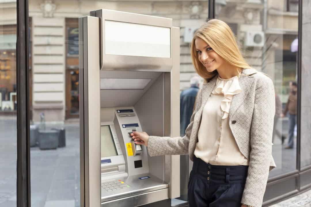 a young blonde woman using ATM machine