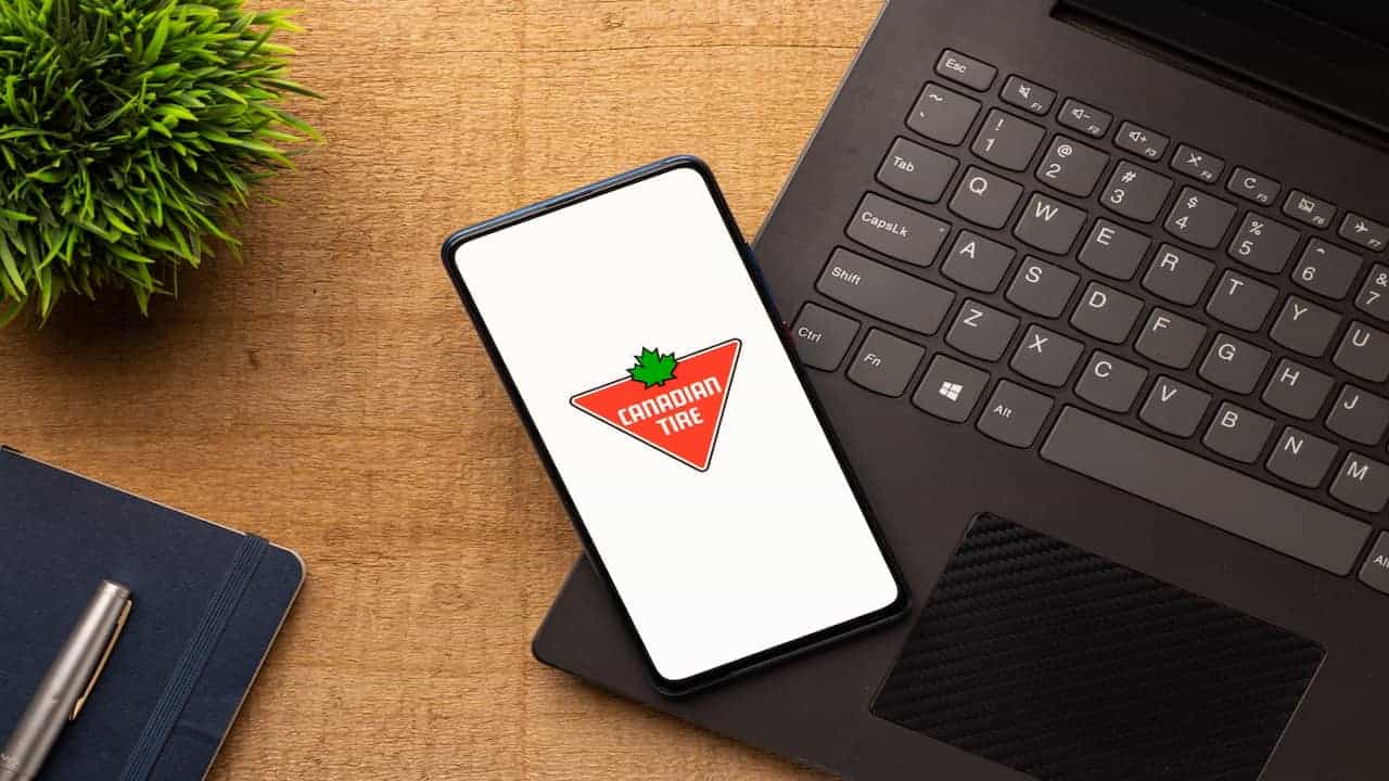 Cellphone with Canadian tire logo on display, a laptop and a plant