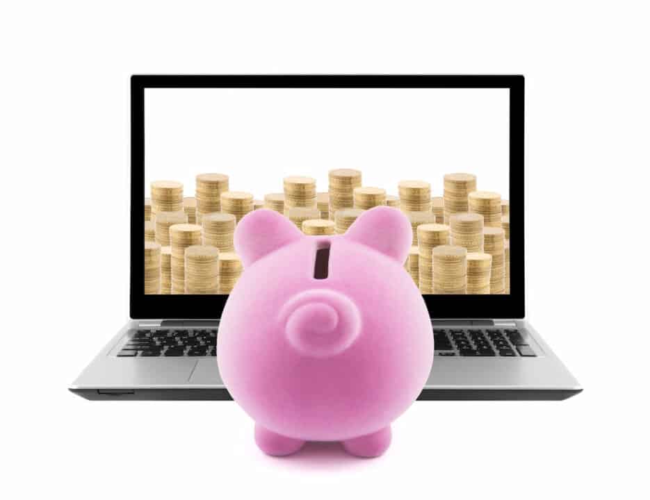 Piggy bank in front of the laptop with coin stacks on the screen