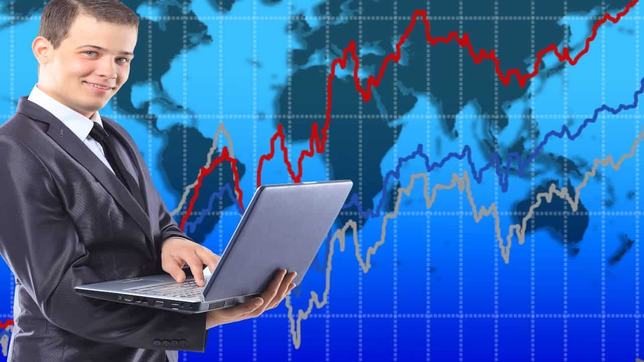 young man with a laptop in front of the big stock graph