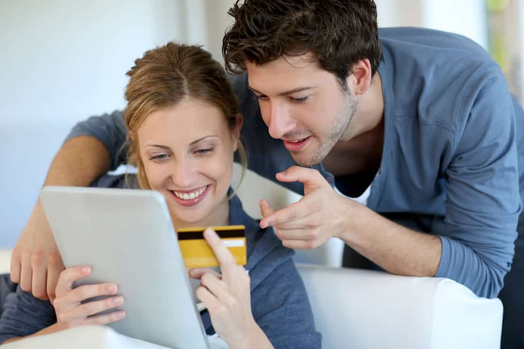 a smiling couple using tablet and credit card