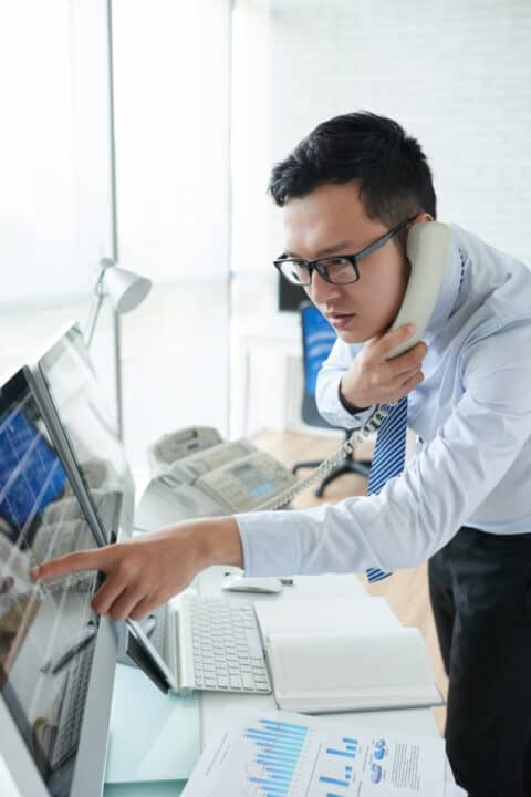 a man standing in front of the computer monitor and using phone