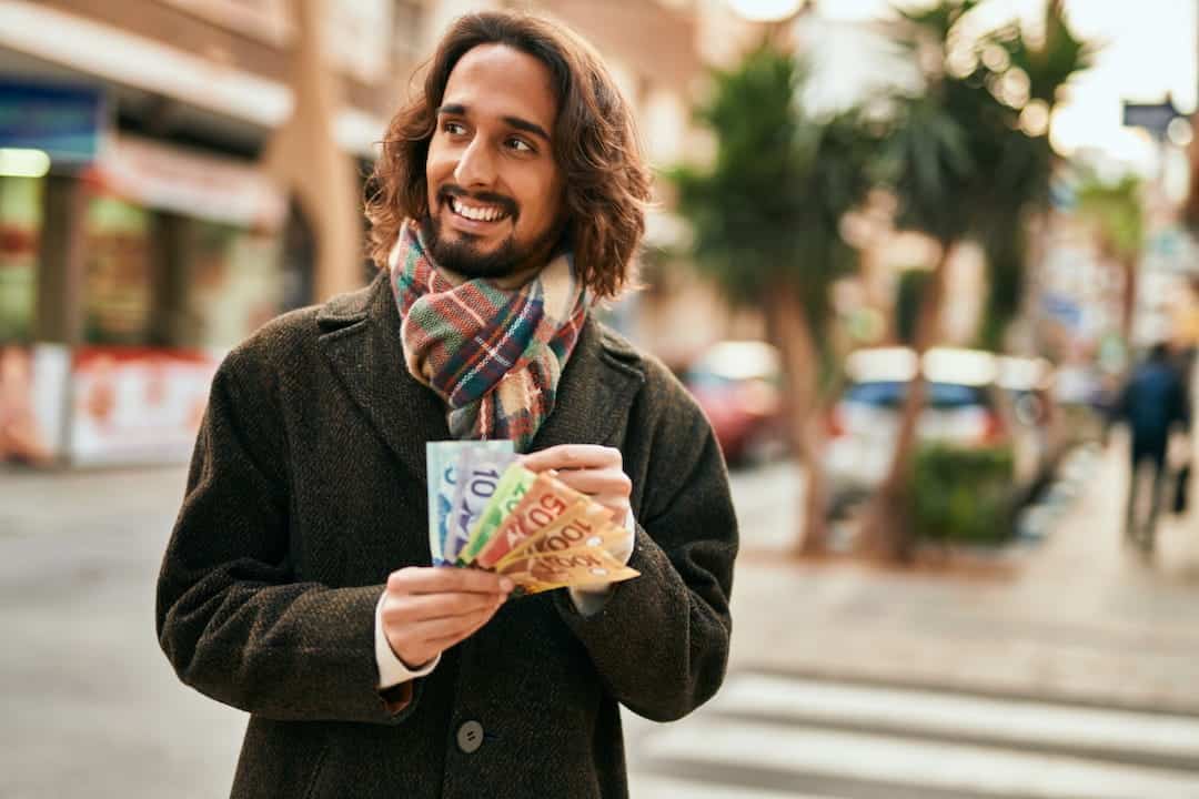 a young smiling man counting money on the street 