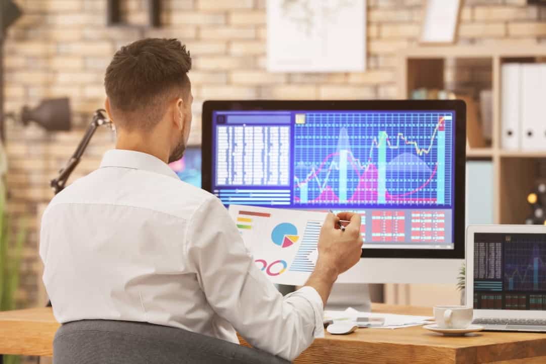 a man in front of the computer monitor trading with stocks