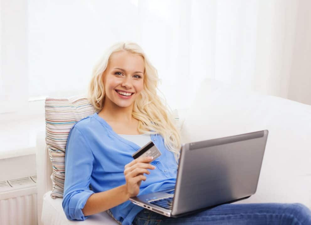 a blonde smiling woman with laptop computer and credit card