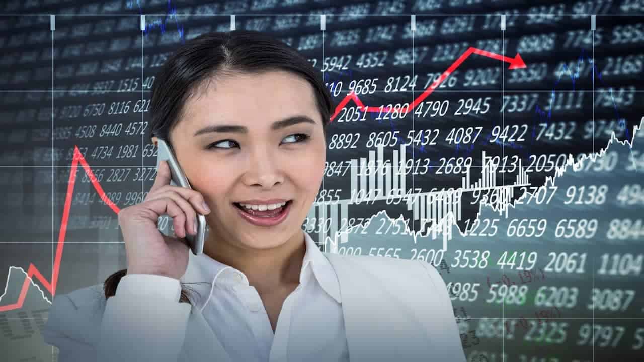 a woman with phone in front of the stock charts