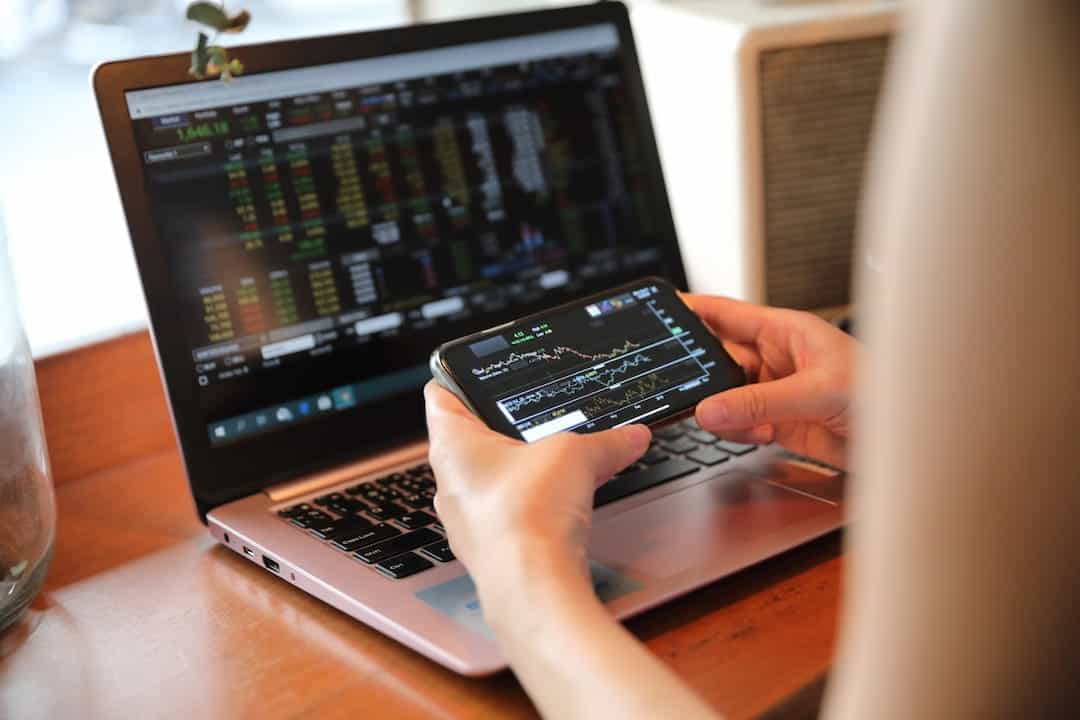 a person watching stock charts on cellphone and laptop screen