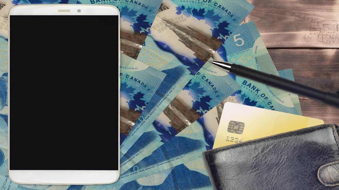 5 Canadian dollars bills and smartphone with purse and credit cards