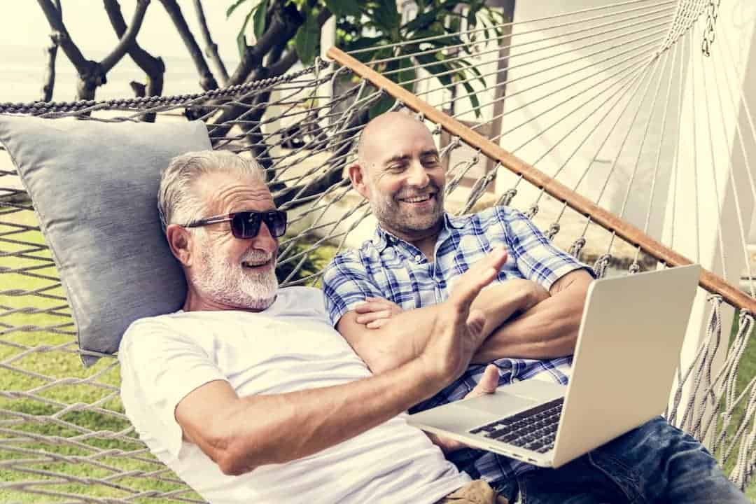 two men looking at the laptop and laughing in a hammock