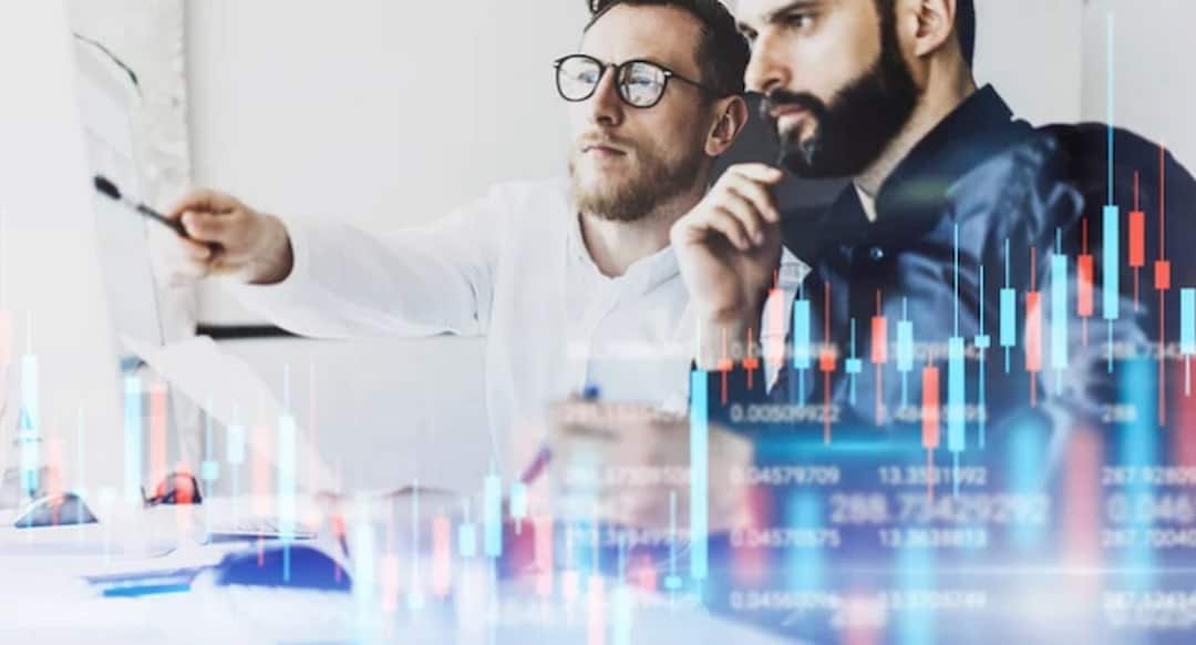 two men looking at the monitor with stock graphs