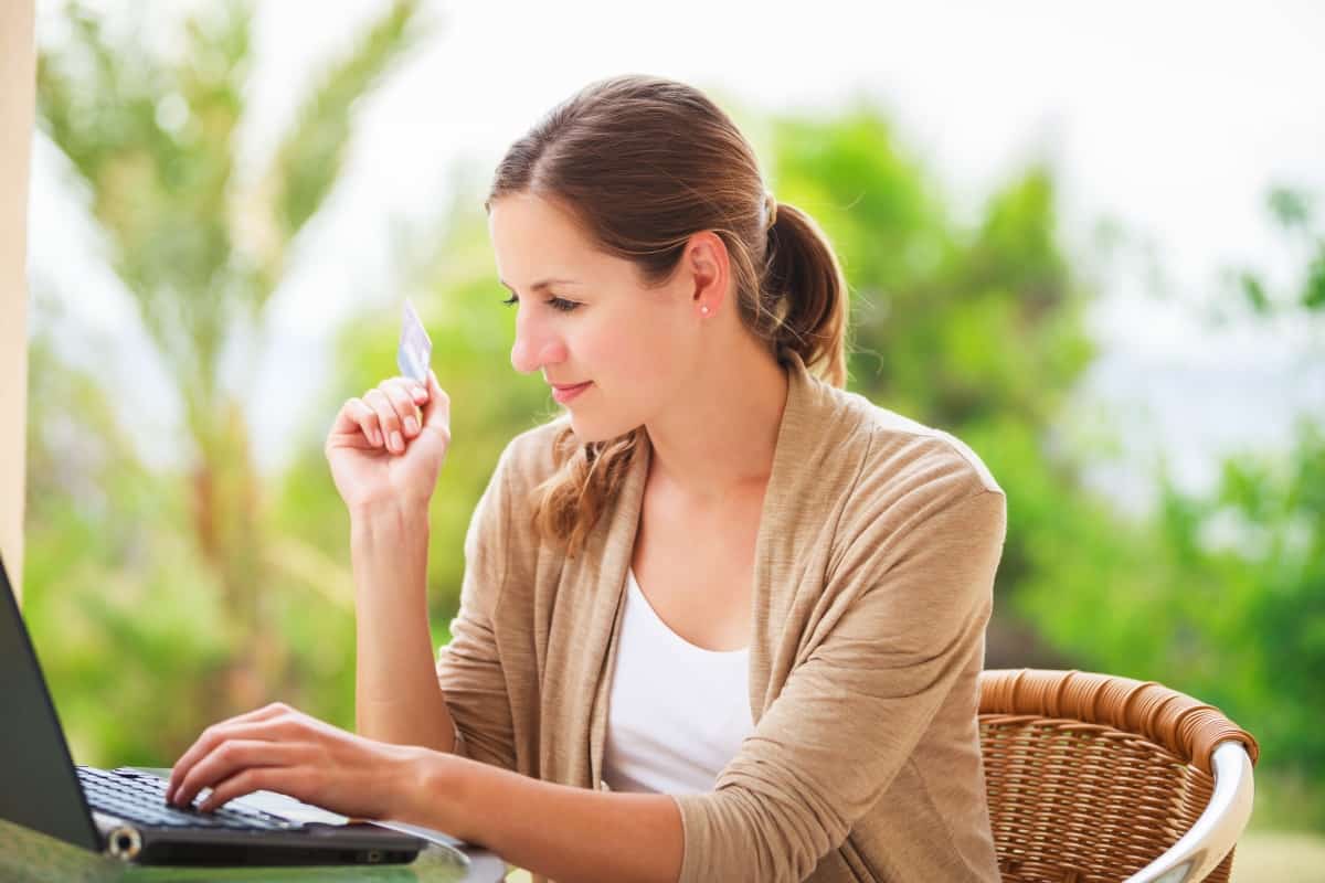 a woman typing on laptop holding plastic credit card in her right hand