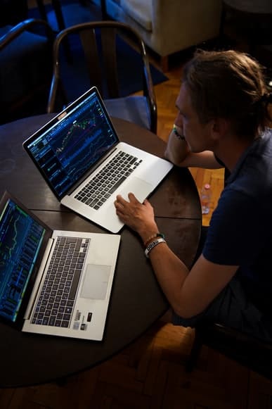 a man watching trading graphs on two laptops
